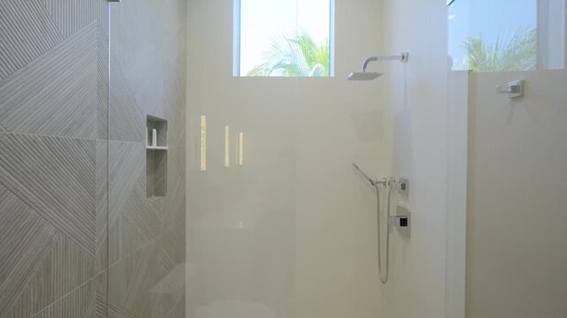 Walk-in shower stall with chrome plumbing, integral shelves for cosmetics and little square window above. Cabinet with transparent glass door and faucet in bathroom