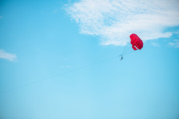A man flies under a red parachute behind a boat, parasailing, sea outdoor activities