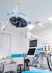 Medical Equipment In Modern Operating Room. A modern operating room with a surgical lamp, a medical monitor, and an examination table.