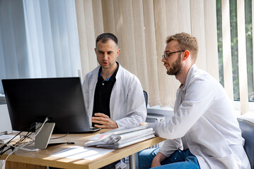 Two Doctors Working On Computer in Office. Two doctors in a medical office discuss something on a...