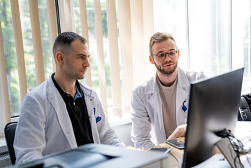 Two Doctors Working on a Computer. Two doctors are sitting at a desk, working on a computer.