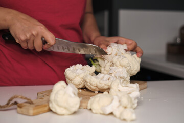 Hands slicing a cauliflower head on a cutting board, highlighting the texture and freshness of the vegetable. This image connects with the trend of healthy cooking and home-prepared meals.