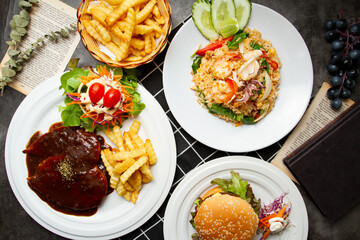 Seafood Fried Rice, Chicken Steak with barbeque sauce, Beef egg and cheese burger, french fries served on plate isolated on table top view of assorted asian food