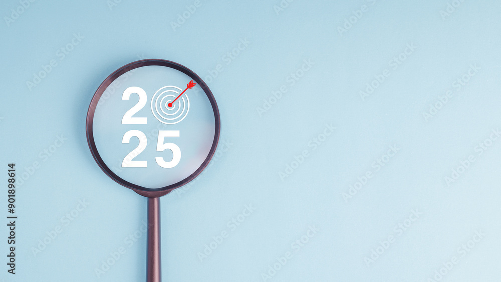Poster a magnifying glass is used to focus on number 2025 with dartboard and red arrow in concept of 2025 n
