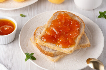 Apricot jam on bread in a white plate and a jar of apricot jam
