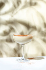 Beige creamy cocktail drink with cognac, liquor, nutmeg and ice. on beige background, hard light