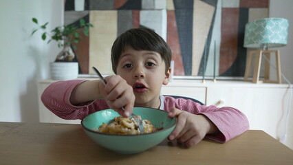 Boy enjoying pasta meal with a fork, emphasizing the joy of eating favorite food, focusing on childhood dining habits and the importance of mealtime, set in a home kitchen environment