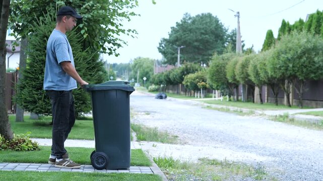 Latino man rolls out a trash can. Garbage collector from a private house