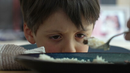 Young boy reluctantly eating rice while being fed by a parent, displaying a range of emotions from hesitation to acceptance