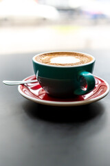 close-up cappuccino in a green cup with a saucer and spoon, set on table with a soft-focus background. image highlights the beverage’s texture and cozy ambiance, perfect for coffee-related content.