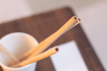 Some bamboo wood straws inside a recyclable paper cup stand out on a blurred background. Reduce plastic waste.
