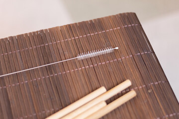 Bamboo cleaning brush next to some out-of-focus reusable straws on a bamboo table