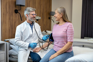 Obraz premium Male doctor checking patients blood pressure and looking concentrated
