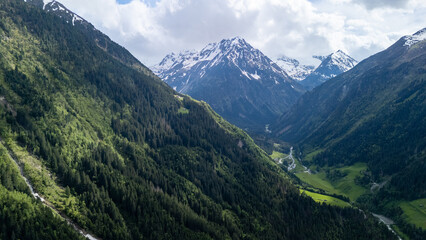 Fototapeta premium Breathtaking Aerial View of Alpine Mountains and Lush Green Valleys Under a Cloudy Sky