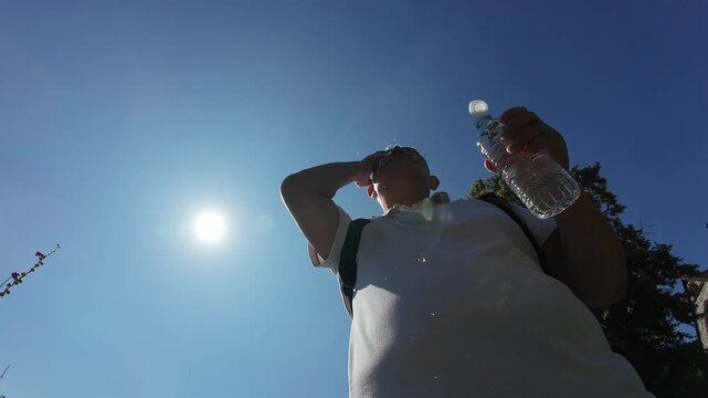 A slow motion low angle clip of a elderly person splashing water on his face to keep cool on a very hot Summer day.