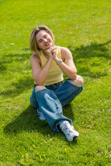 Young adult woman enjoying a sunny day in the park sitting and smiling on green grass