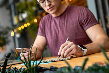 Cropped shot of young businessman manager freelancer student holding using smart phone and making notes at coworking while working remote studding distant learning online. Education business concept