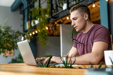 Thoughtful caucasian young man student freelancer manager worker typing on laptop doing project while working remote distant studding learning online at coworking office. Education business concept