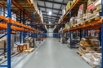View of a Spacious Warehouse Aisle Filled With Stacked Pallets and Boxes in Bright Lighting.The...