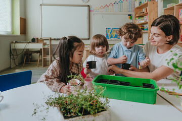 Young woman teacher with children in kindergarten plants a plant in a pot