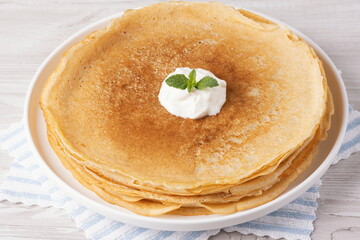 Pancakes with sour cream on a white wooden table