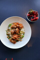 Orange chicken and rice dish with a side bowl of mixed berries