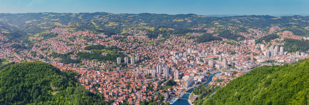 Aerial panorama of Uzice, Serbia, showcasing the cityscape with its urban architecture, green hills, and surrounding mountains
