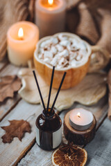 Autumn home perfume in glass bottle with wooden sticks, scented candles as apartment air freshener. Pumpkin sweet latte fragrance, spices, cinnamon, anise. Aromatherapy, cozy atmosphere, comfort