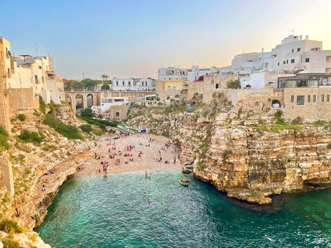 Experience summer at Lama Monachile in Polignano a Mare, Italy. Nestled between cliffs and white-washed buildings, the turquoise waters and historic Roman bridge make this cove a picturesque retreat.
