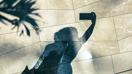 A woman takes a selfie and a shadow silhouette of her is on the ground.