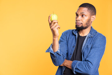 African american zero waste enthusiast holds a green apple in the studio, enjoying raw vegan nutrition with ethically sourced ripe fruits. Advertising additives free organic produce.