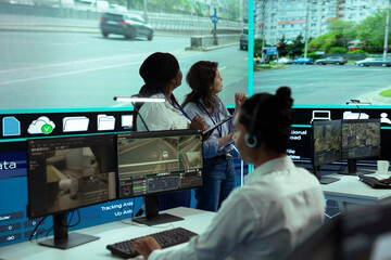 Diverse experts following city traffic on a display in monitoring room, reviewing CCTV radar video footage. Agency employees working on surveillance and collecting license plate data.