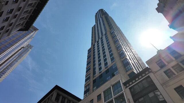 Summer sunlight peeks from behind tall midtown Manhattan skyscrapers on a clear blue sky summer day.	