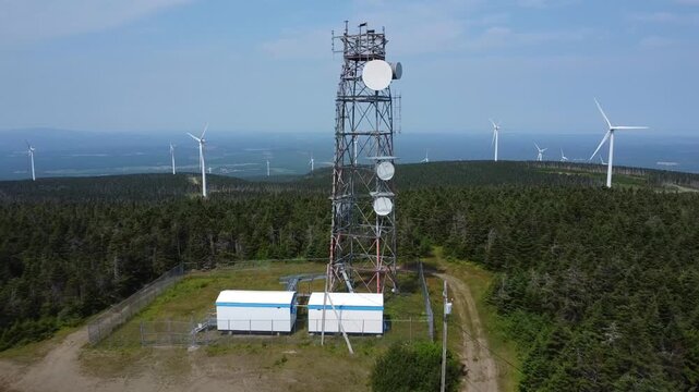 Envol&eacute; d'un drone autour d'une tour de communication et d'antennes cellulaires entour&eacute;e d'&eacute;oliennes au sommet de montagnes verdoyantes. Parc &eacute;olien du Lac Alfred, Qu&eacute;bec, Canada.