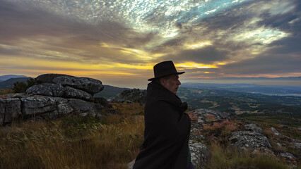 silhouette of man with contemplates the sunrise dressed in a cape and hat