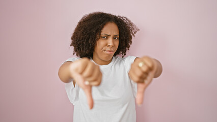 African american woman with braids giving thumbs down against pink background