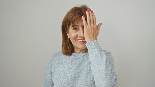 Mature woman covering one eye with hand against a white background, portraying playfulness or vision concept.