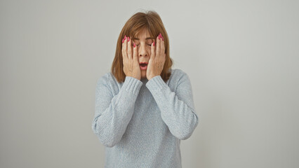 Stressed middle-aged woman with short hair covering face with hands against a white background.