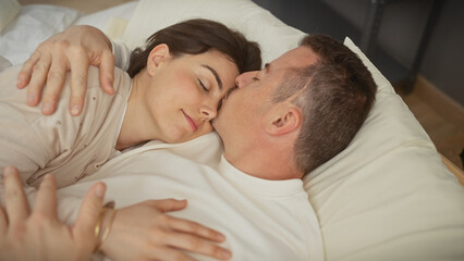 Couple embracing in love on a cozy bed at home, portraying a sense of romance, intimacy, and comfort between a man and woman in a private interior setting.