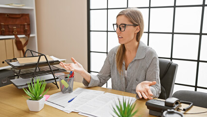 A professional young woman engages in an animated conversation in a modern office setting with paperwork.