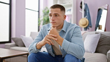 Thoughtful young hispanic man sitting in a modern living room interior.