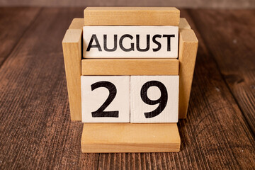 Wooden block calendar with the date August 29 and spikelets of wheat on a beige concrete background.