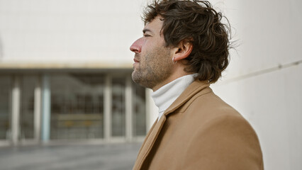 A stylish hispanic man in a coat looks thoughtfully across a modern urban environment, evoking a...