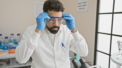 Fototapeta premium A man adjusts his safety goggles in a brightly lit laboratory, symbolizing research and healthcare.