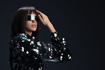 Woman in sequinned top, holding her hands to her face, eyes closed, looking at the camera,...