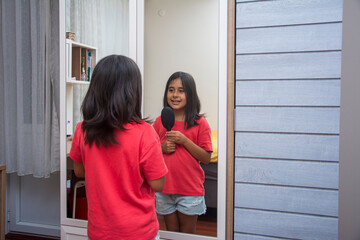 Primary school girl sings in front of the mirror, using a comb as a microphone