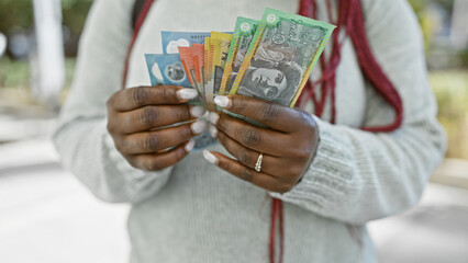 A woman with braids holds australian currency on a city street, emphasizing commerce and urban life.