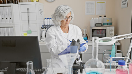 Mature woman scientist analyzing samples in a laboratory setting, with professional equipment indoors.