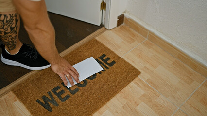 A man reaches for an envelope on a 'welcome' doormat inside a house, hinting at a personal story or communication