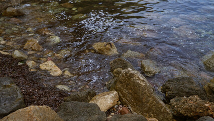 Rocky shore with water gently lapping against various sized rocks and pebbles, creating a serene natural coastal scene.